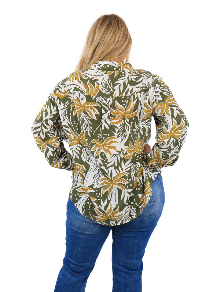 Mujer vistiendo camisa de botones con estampado de hojas tropicales en colores verde, mostaza y blanco.