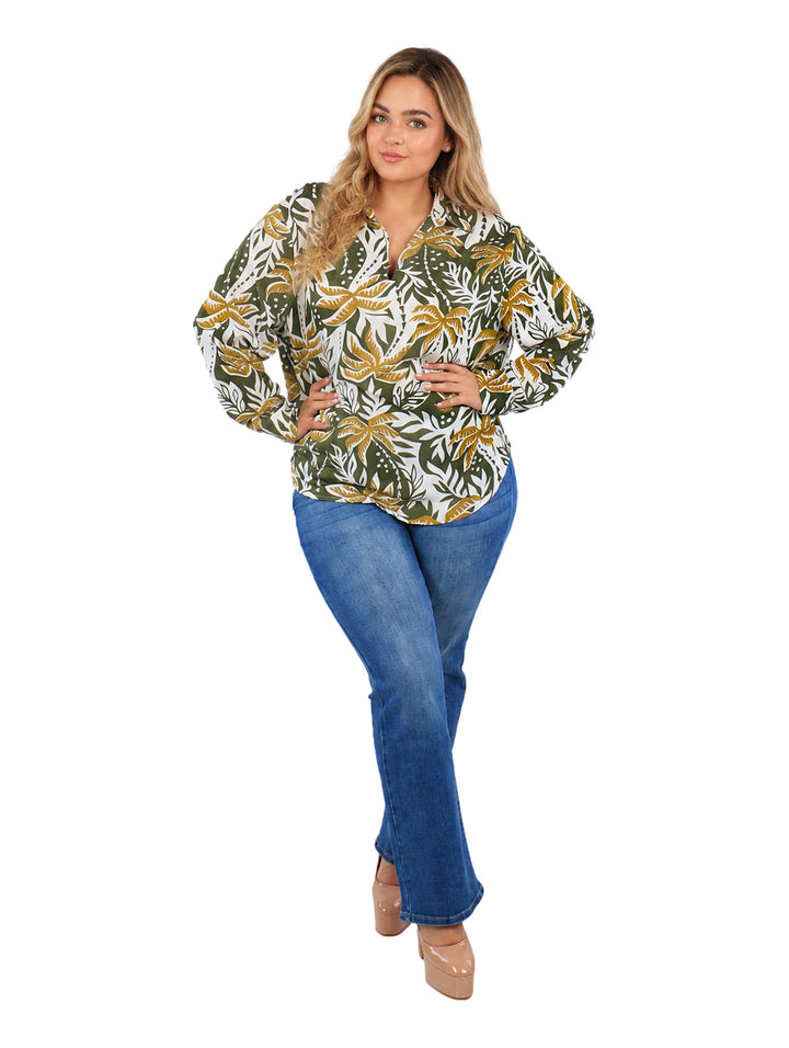 Mujer vistiendo camisa de botones con estampado de hojas tropicales en colores verde, mostaza y blanco.