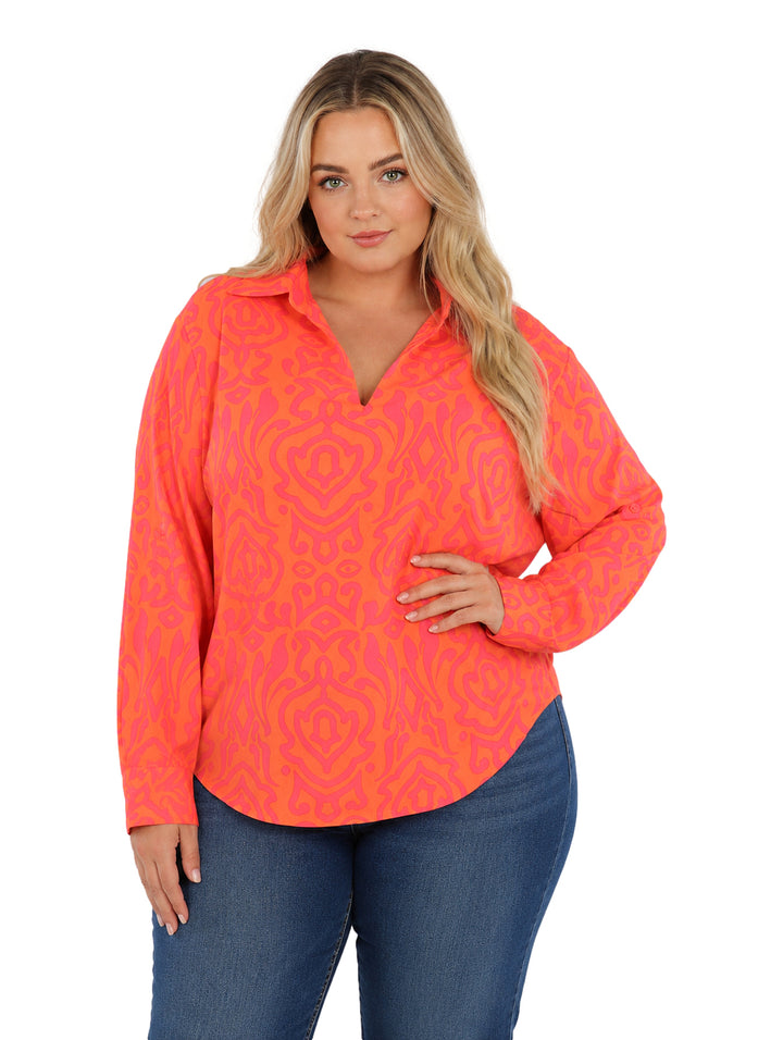 Mujer vistiendo camisa de botones con estampado abstracto en tonos naranja y rosa, de corte amplio y manga larga.