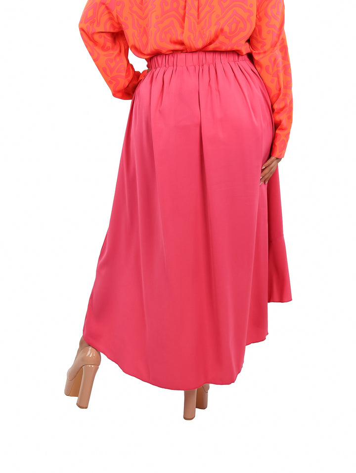 Mujer vistiendo falda satinada color magenta de corte largo con abertura frontal y detalles de volantes.