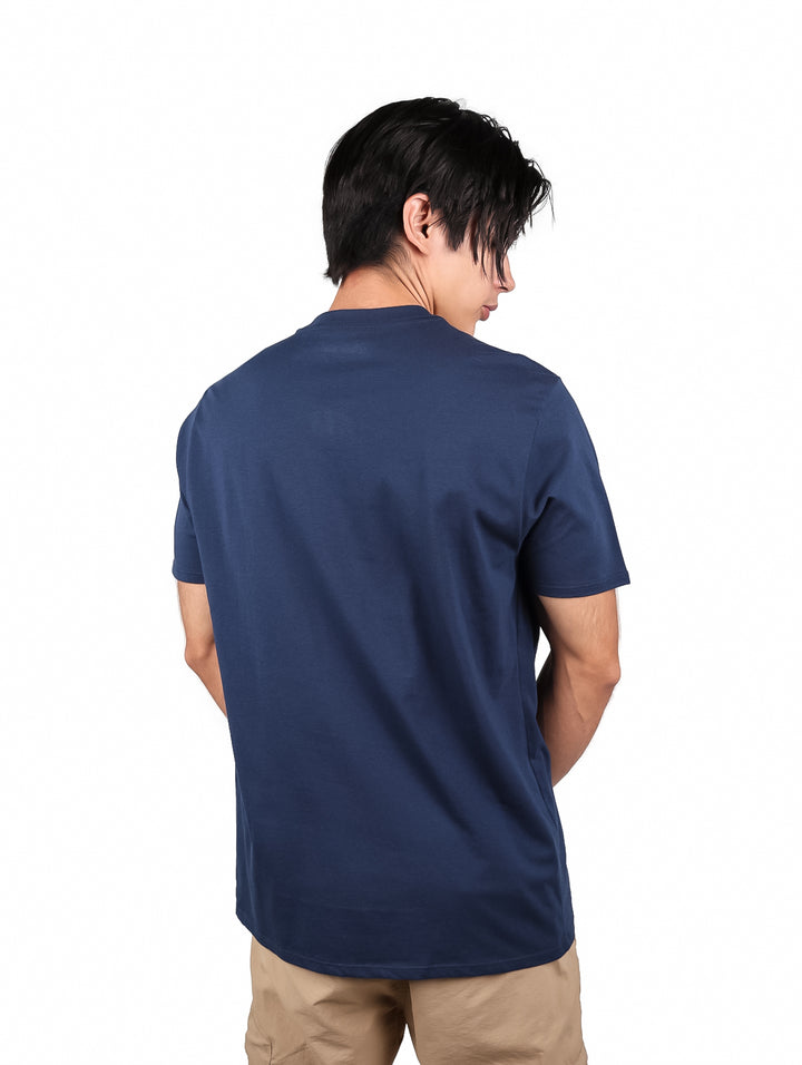 Hombre vistiendo playera Wrangler color marino con estampado circular en el pecho y pantalones beige.
