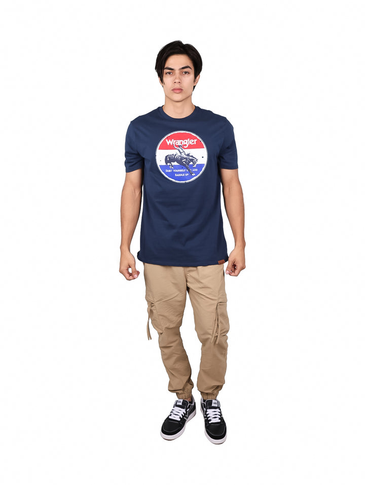 Hombre vistiendo playera Wrangler color marino con estampado circular en el pecho y pantalones beige.