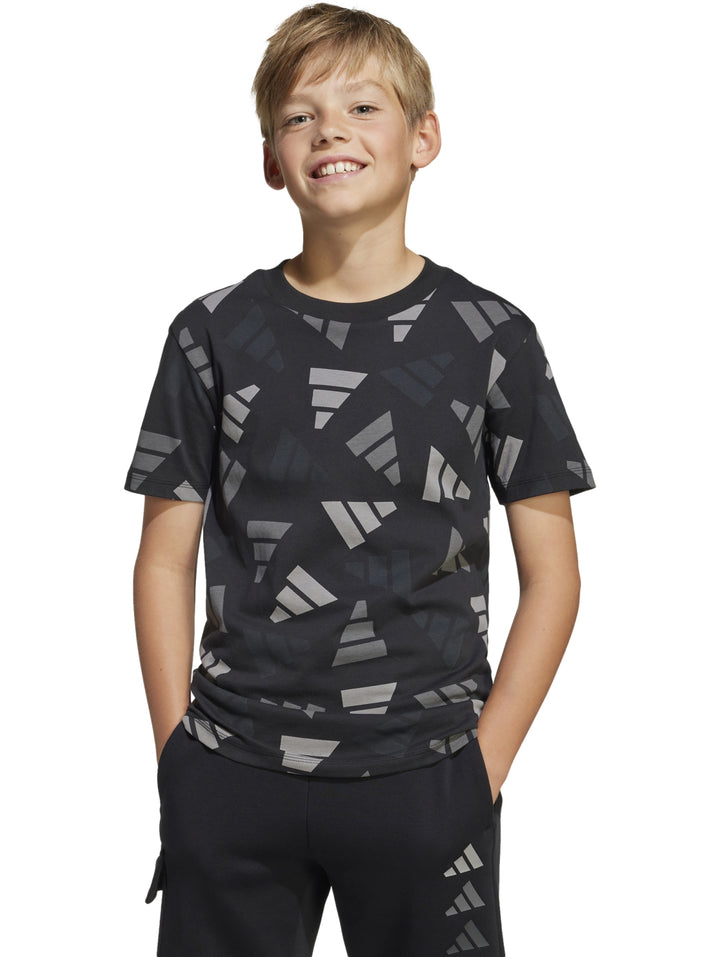 Niño vistiendo playera Adidas negra con estampado geométrico en gris y pantalones negros.
