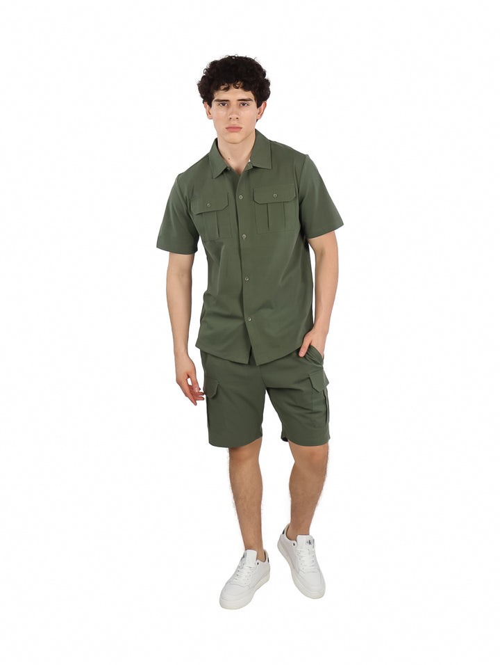 Hombre vistiendo un conjunto de camisa y short color verde militar con tenis blancos.