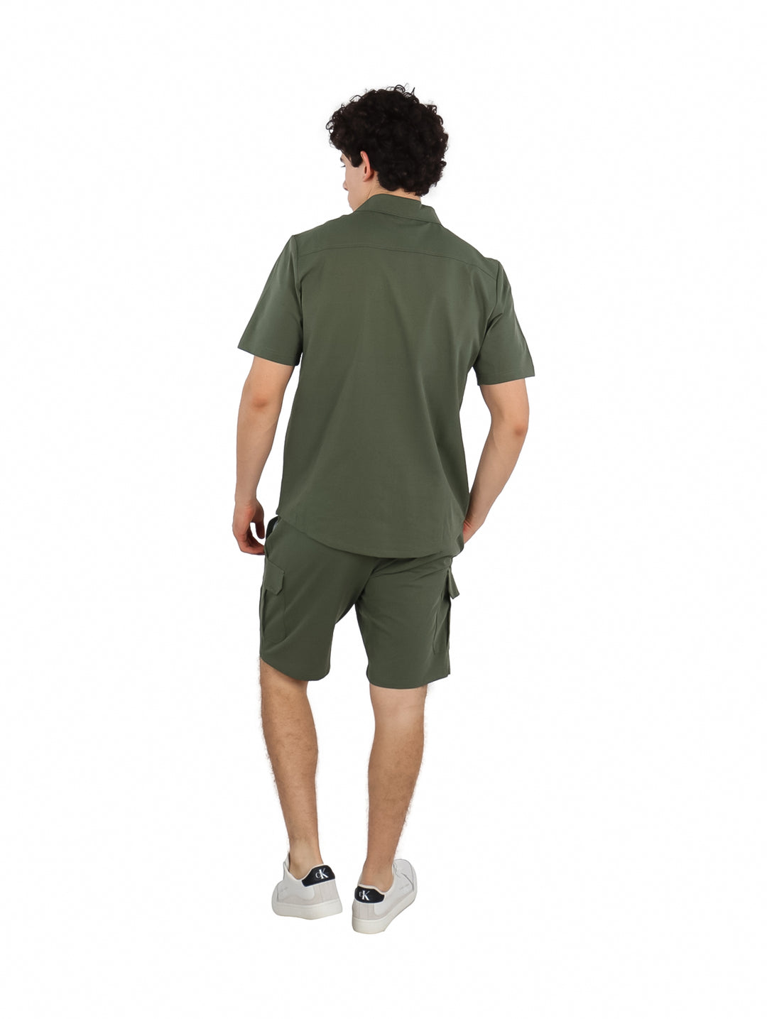 Hombre vistiendo un conjunto de camisa y short color verde militar con tenis blancos.