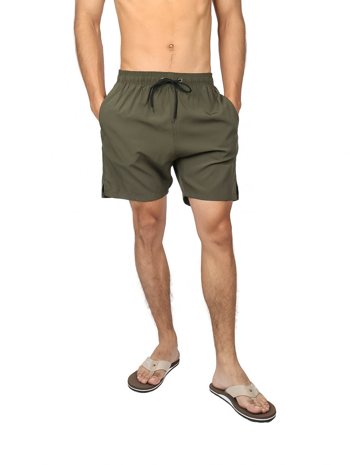 Hombre vistiendo traje de baño corto color verde militar con cordón ajustable en la cintura.