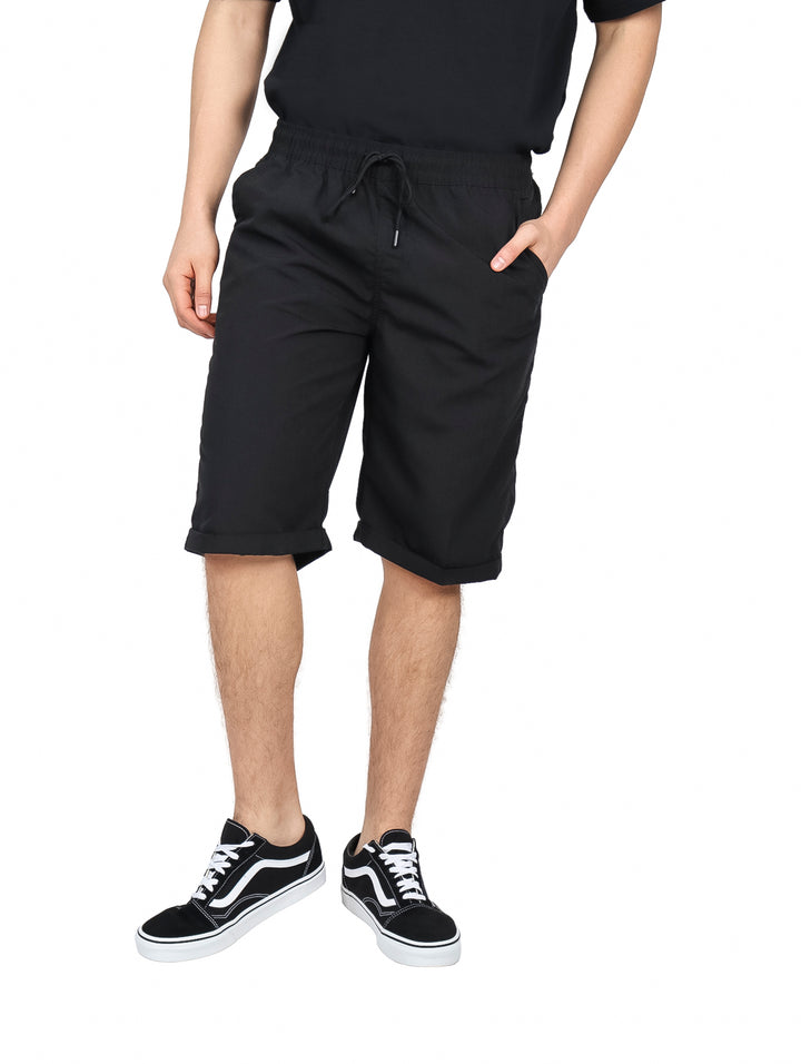 Hombre vistiendo bermuda negra de cintura elástica con cordón y calzado deportivo negro y blanco.