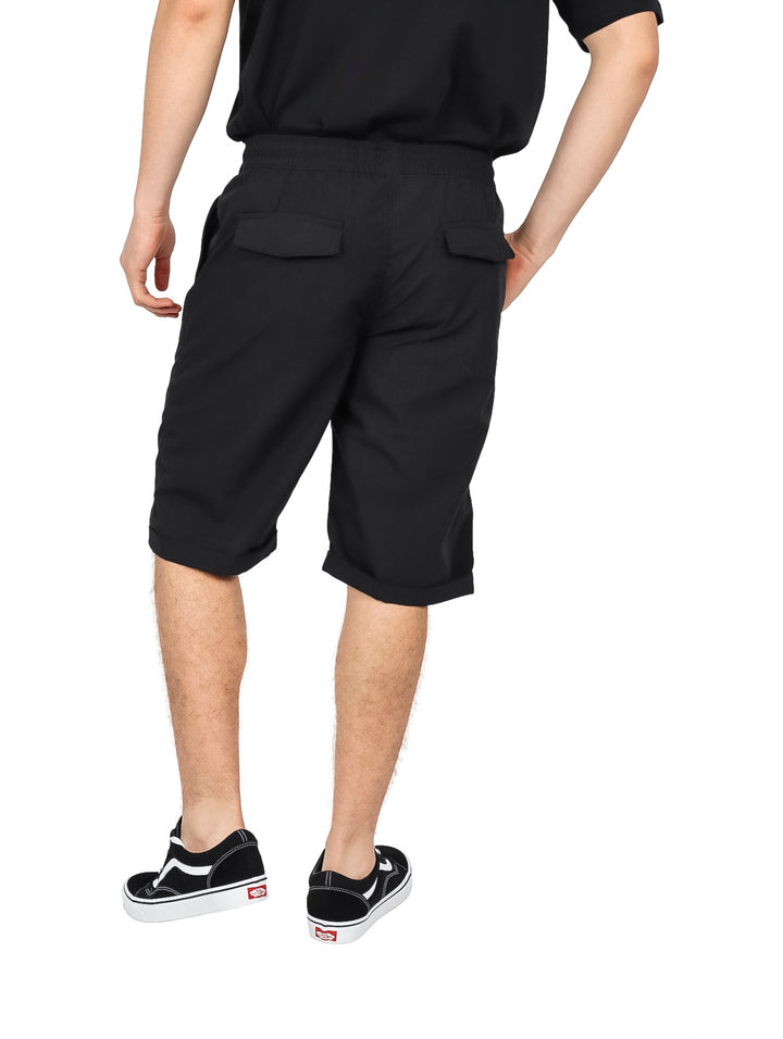 Hombre vistiendo bermuda negra de cintura elástica con cordón y calzado deportivo negro y blanco.