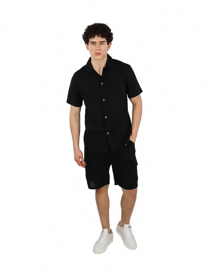 Hombre vistiendo un conjunto casual de camisa y shorts color negro con tenis blancos.