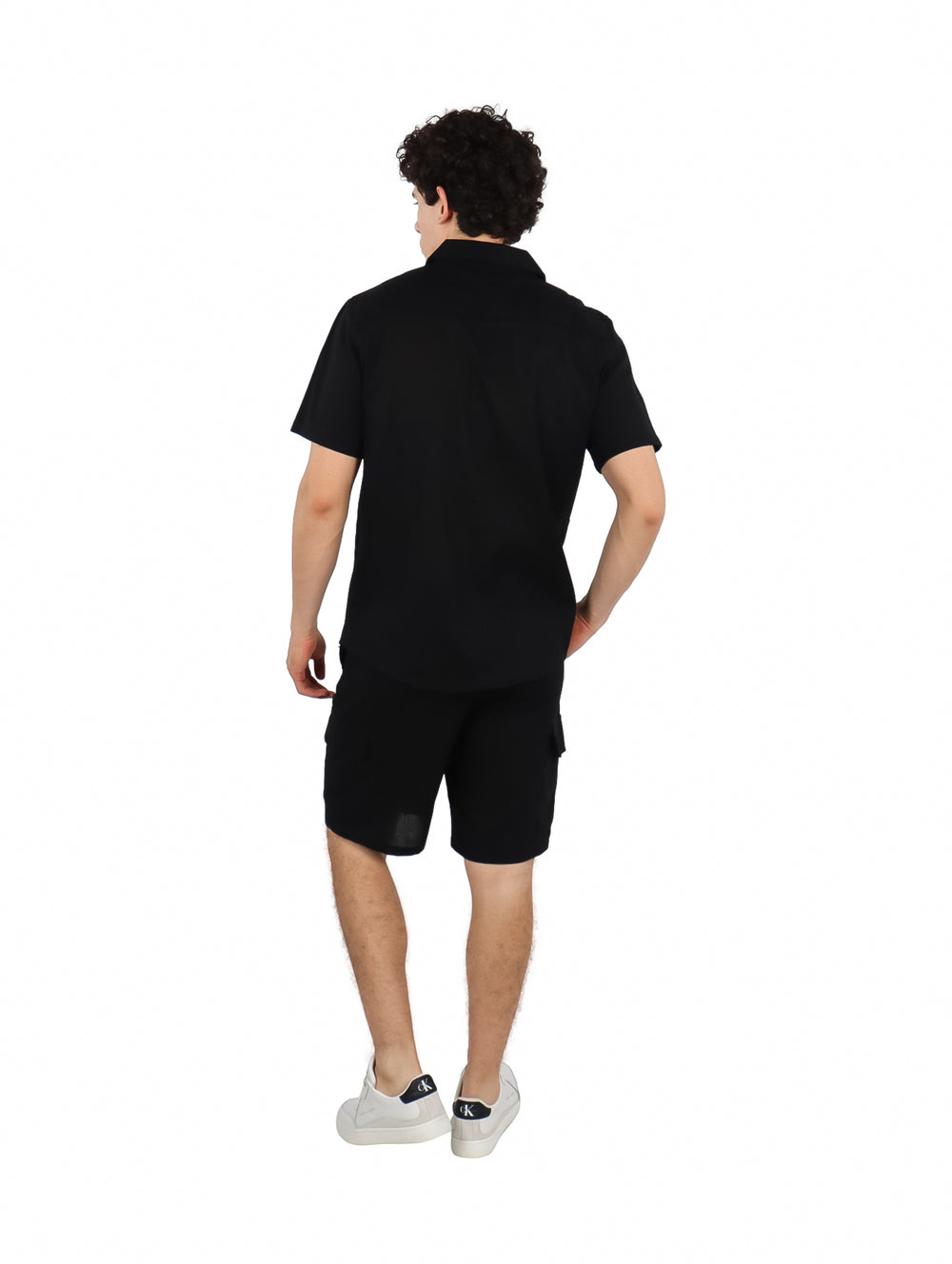 Hombre vistiendo un conjunto casual de camisa y shorts color negro con tenis blancos.