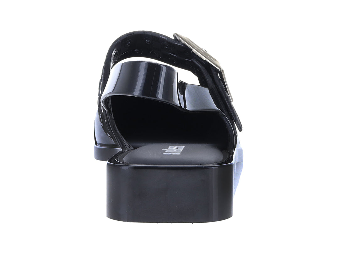 Zapato plano negro brillante de punta afilada con correa y hebilla dorada.