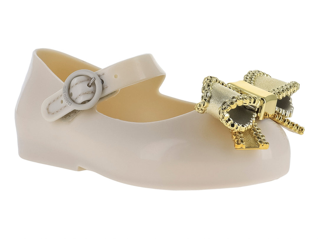 Zapato infantil Mini Melissa color beige con moño dorado y correa ajustable.