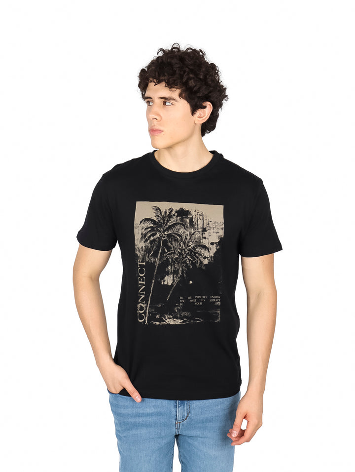 Hombre vistiendo una camiseta negra de manga corta con un estampado gráfico beige de palmeras en el pecho.