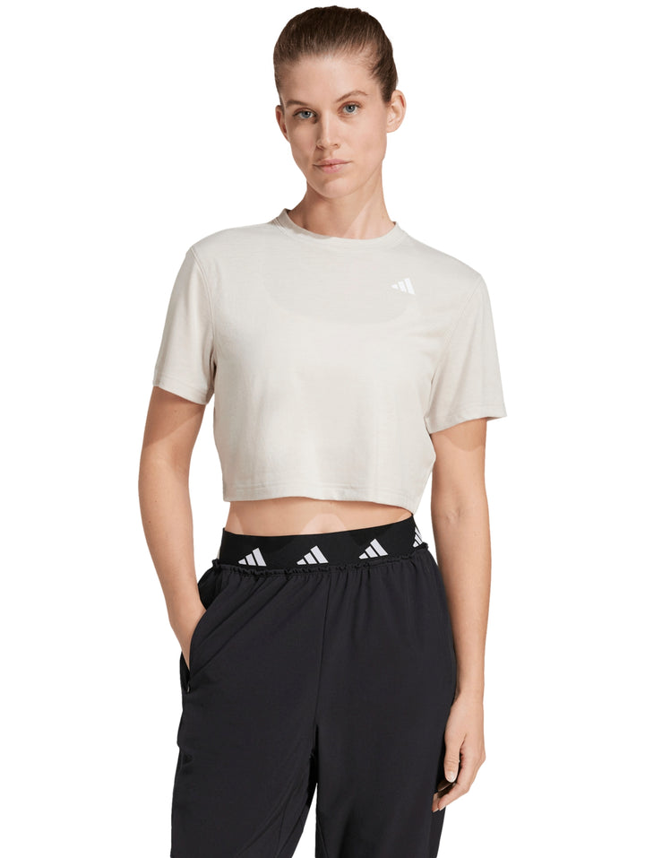 Mujer vistiendo camiseta de entrenamiento Adidas color beige con corte boxy y cuello redondo.