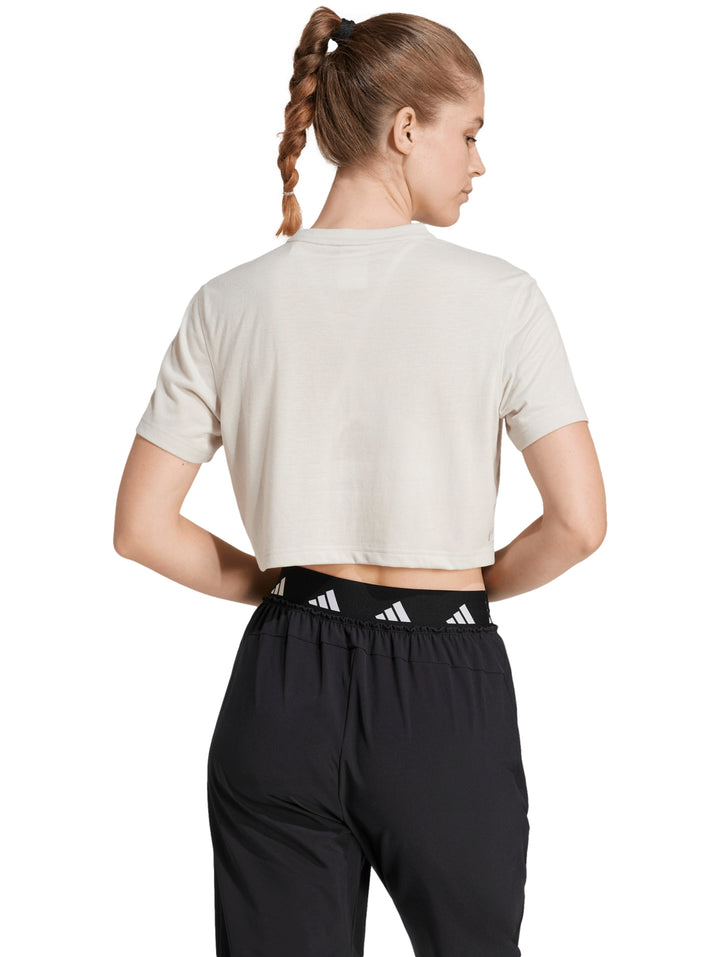 Mujer vistiendo camiseta de entrenamiento Adidas color beige con corte boxy y cuello redondo.