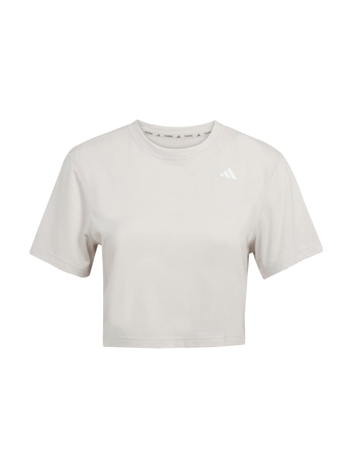 Mujer vistiendo camiseta de entrenamiento Adidas color beige con corte boxy y cuello redondo.
