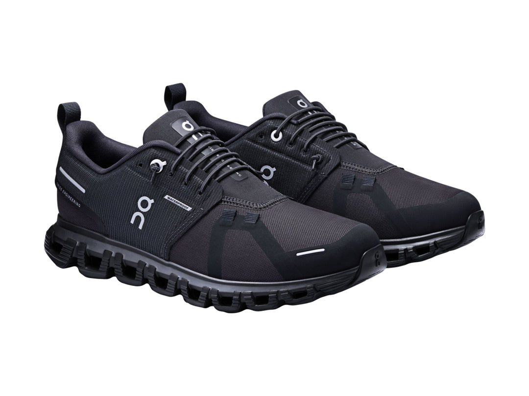 Tenis deportivos On Cloud color negro con suela amortiguada característica y detalles en blanco.
