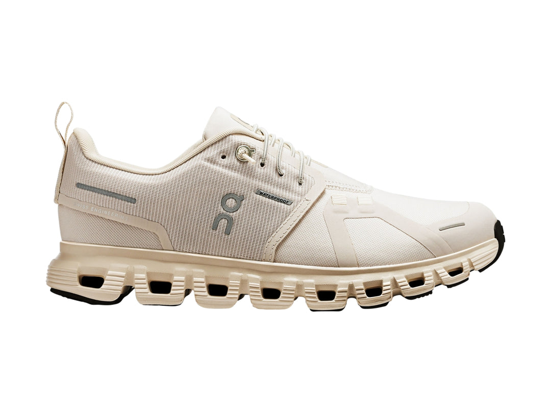 Tenis deportivos On Cloud color crema con suela amortiguada y detalles en gris.