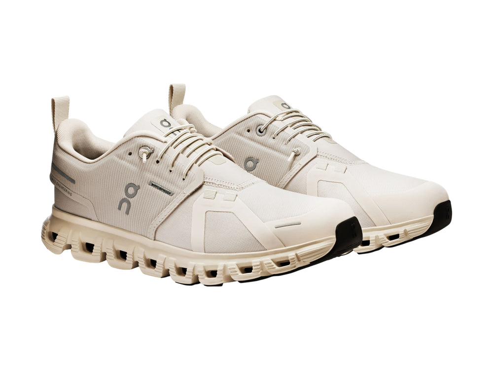 Tenis deportivos On Cloud color crema con suela amortiguada y detalles en gris.