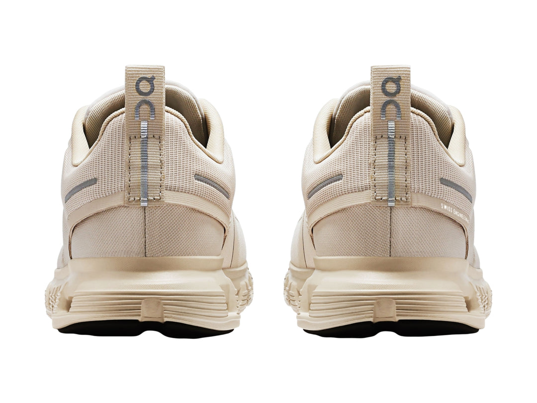 Tenis deportivos On Cloud color crema con suela amortiguada y detalles en gris.