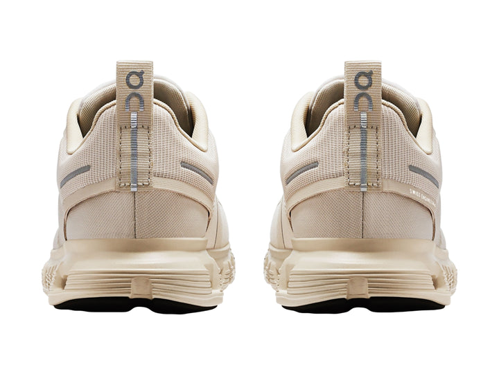 Tenis deportivos On Cloud color crema con suela amortiguada y detalles en gris.
