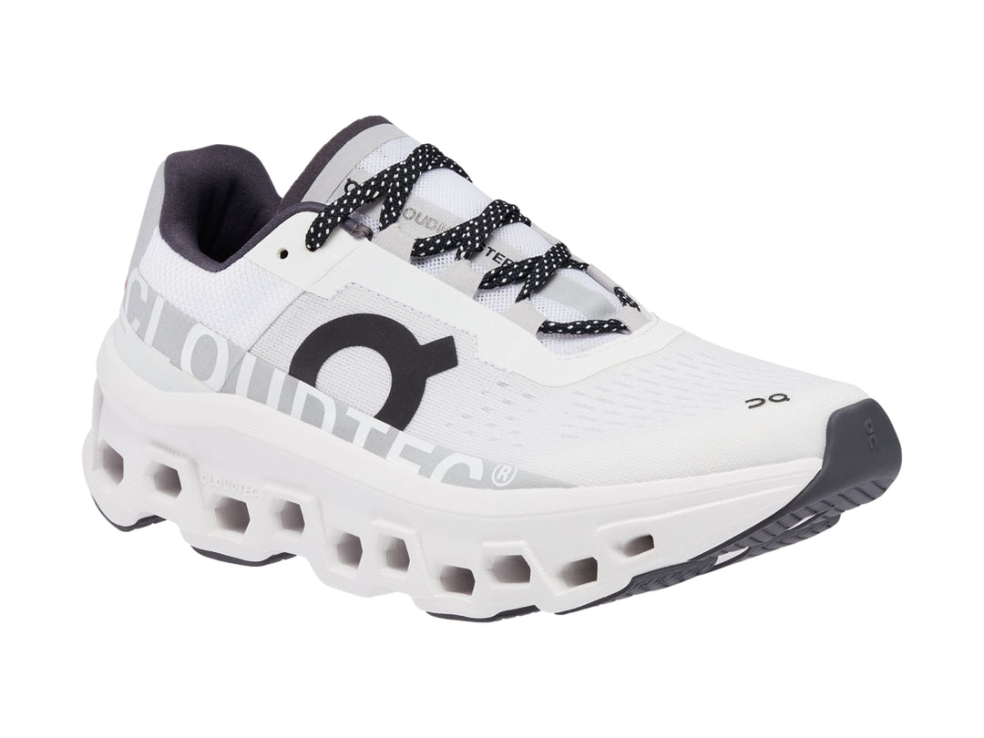 Tenis deportivos On Cloudmonster color blanco con detalles negros y suela amortiguada.