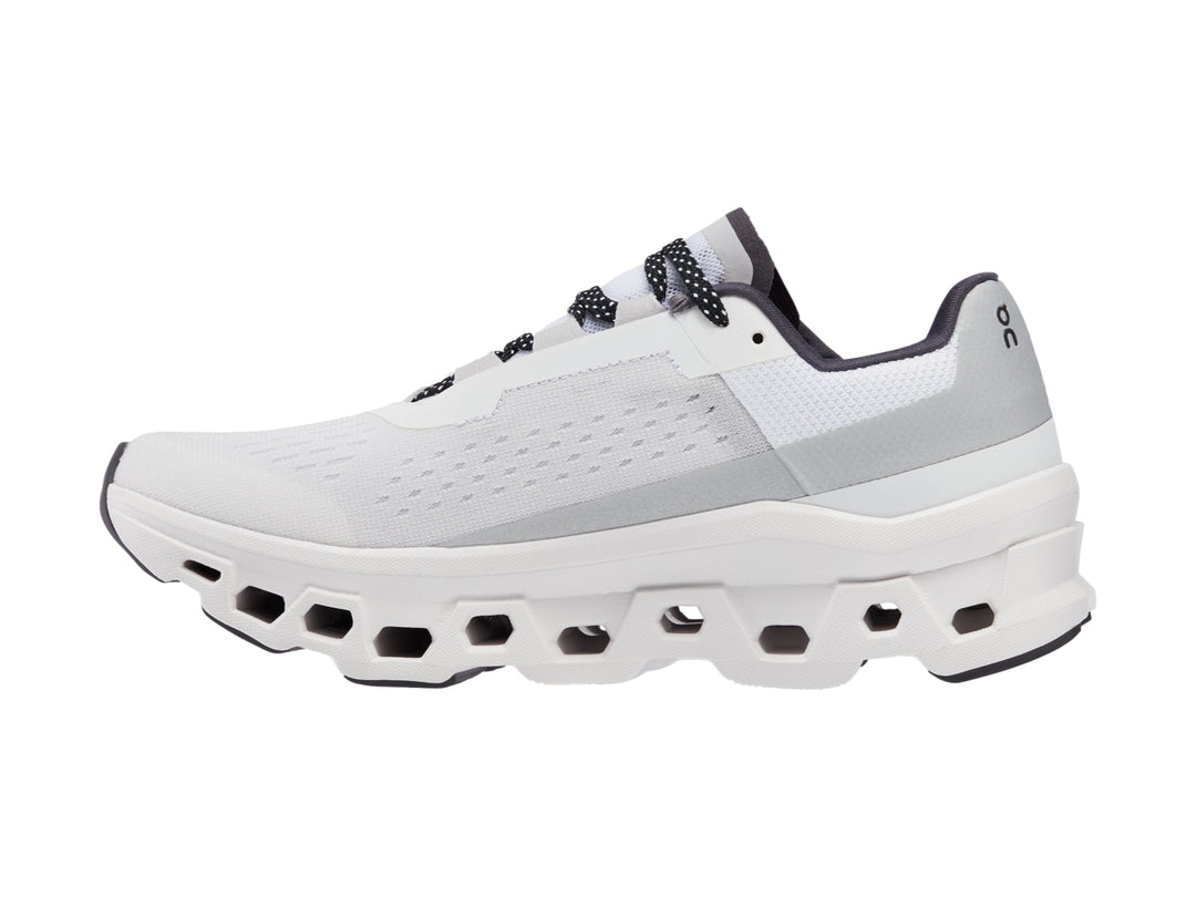 Tenis deportivos On Cloudmonster color blanco con detalles negros y suela amortiguada.