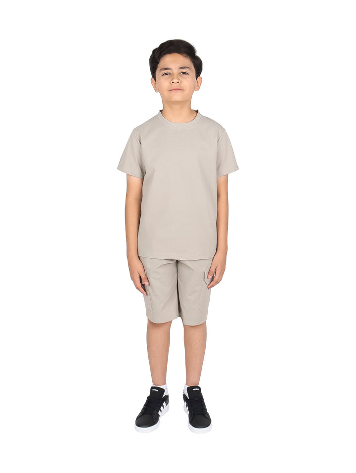 Niño vistiendo un conjunto casual de camiseta y short en color beige con tenis negros.