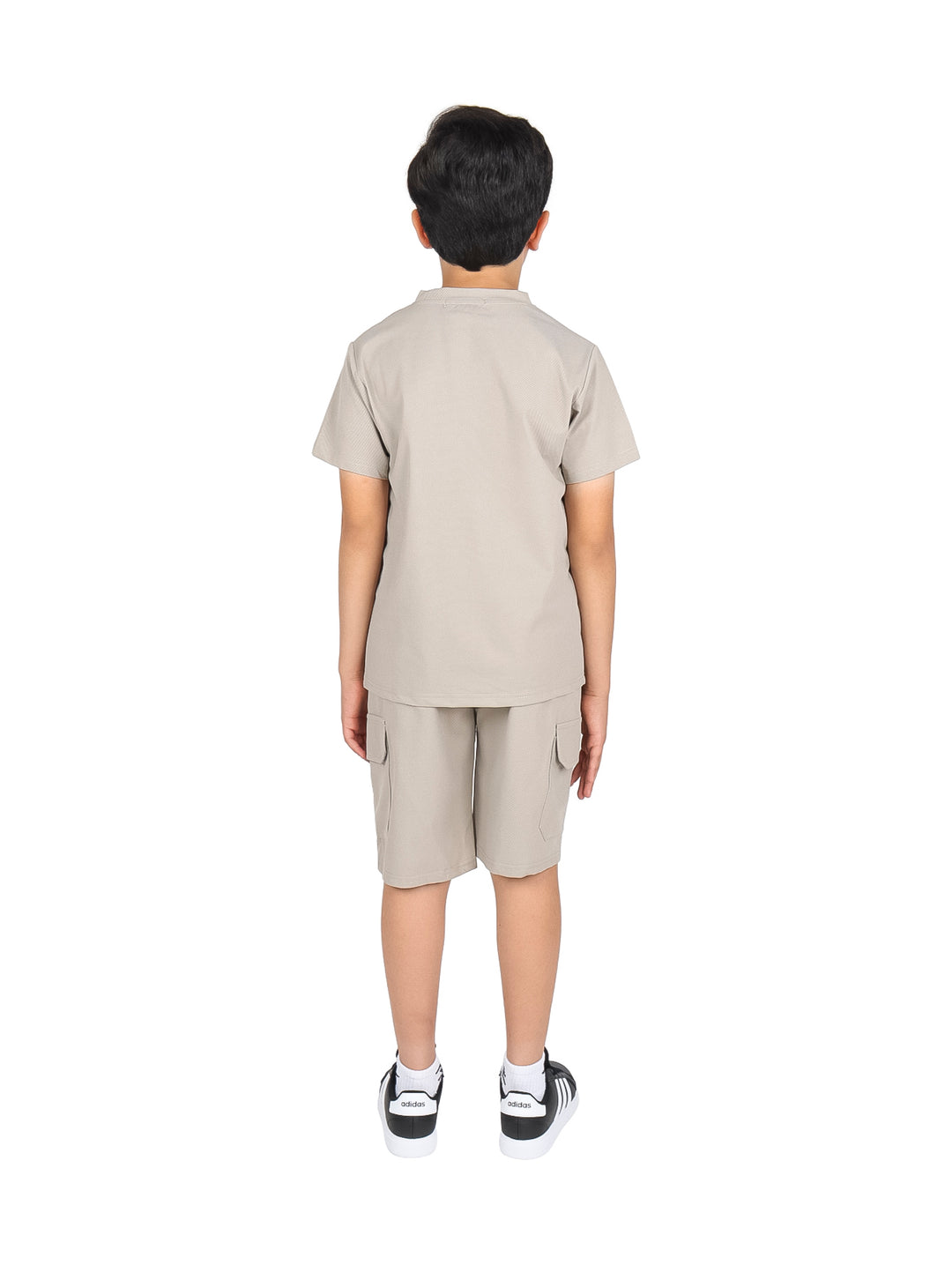 Niño vistiendo un conjunto casual de camiseta y short en color beige con tenis negros.