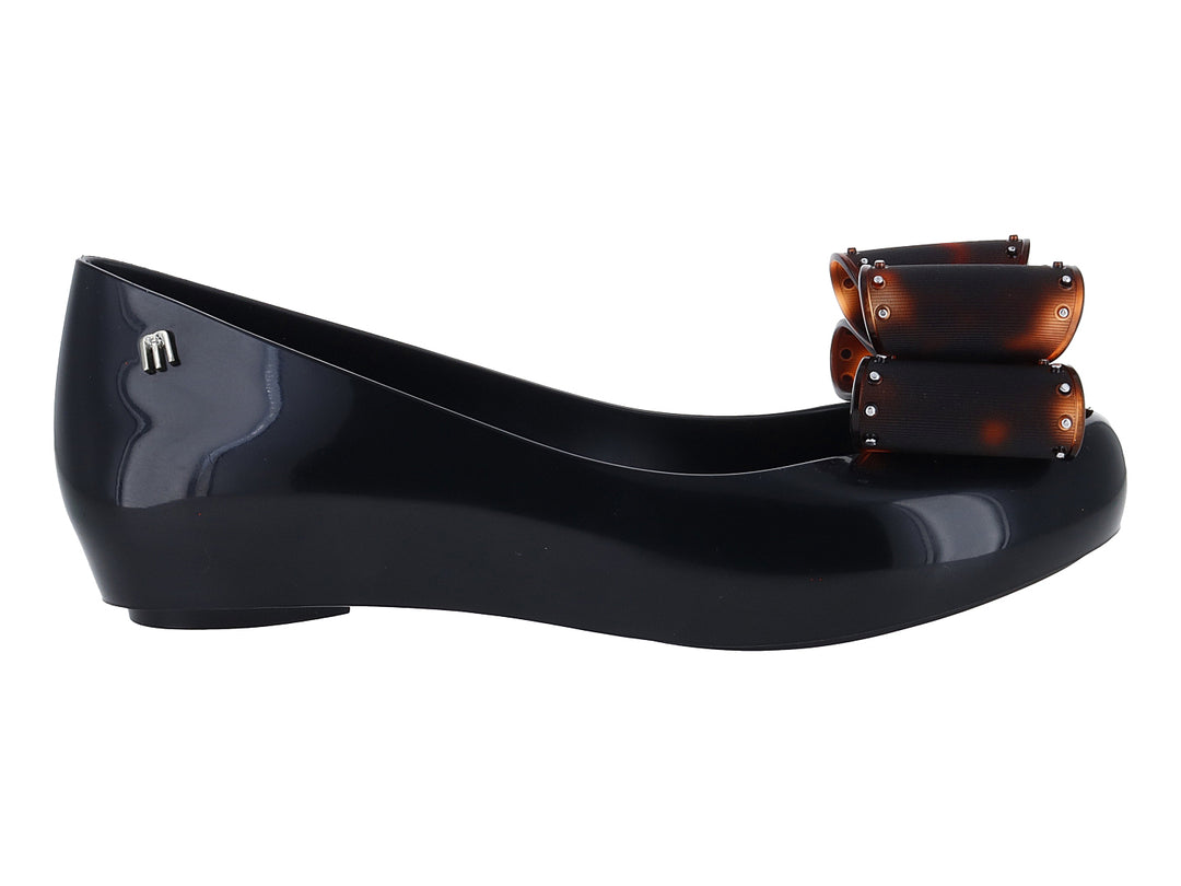 Zapato plano negro de marca Melissa con plataforma y un moño decorativo en color marrón brillante.