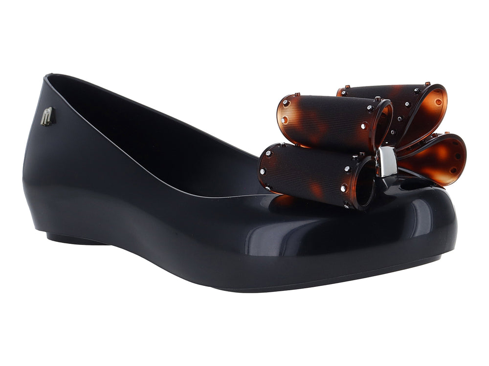 Zapato plano negro de marca Melissa con plataforma y un moño decorativo en color marrón brillante.