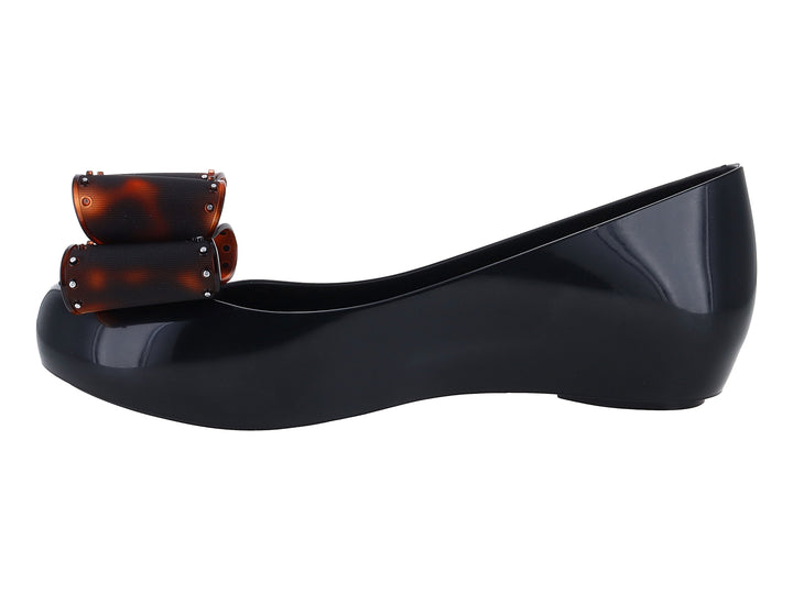 Zapato plano negro de marca Melissa con plataforma y un moño decorativo en color marrón brillante.