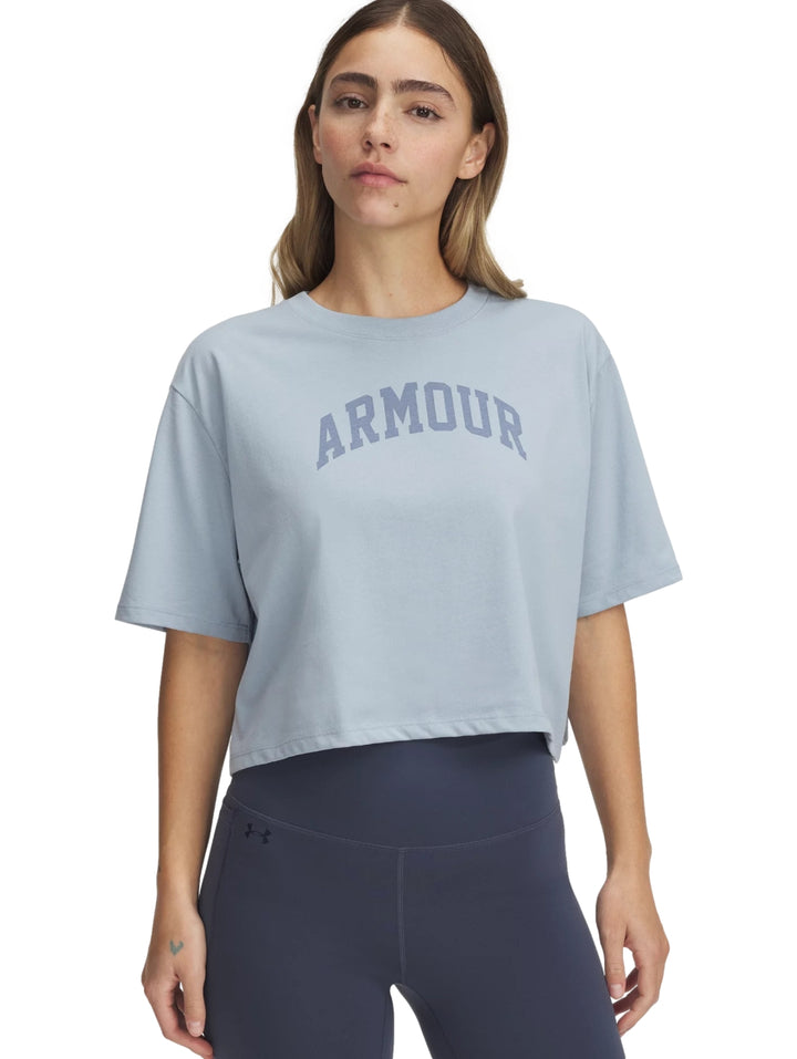 Mujer vistiendo una camiseta corta color gris de Under Armour con la palabra ARMOUR impresa en el pecho.