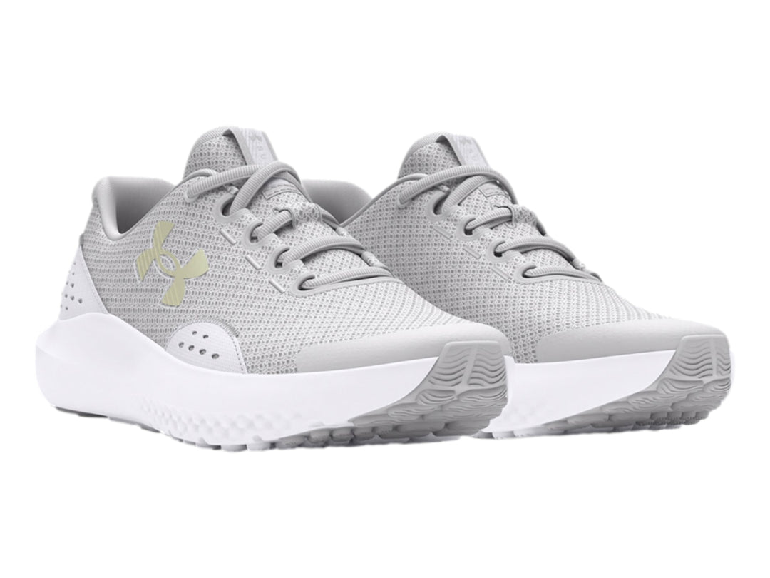 Tenis deportivos Under Armour color gris con suela blanca y logotipo dorado en el costado.