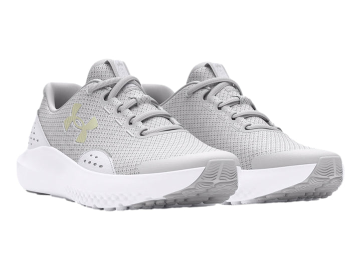 Tenis deportivos Under Armour color gris con suela blanca y logotipo dorado en el costado.