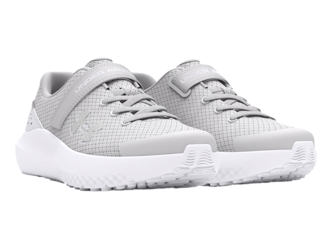 Tenis deportivos Under Armour color gris con suela blanca y correa de ajuste.