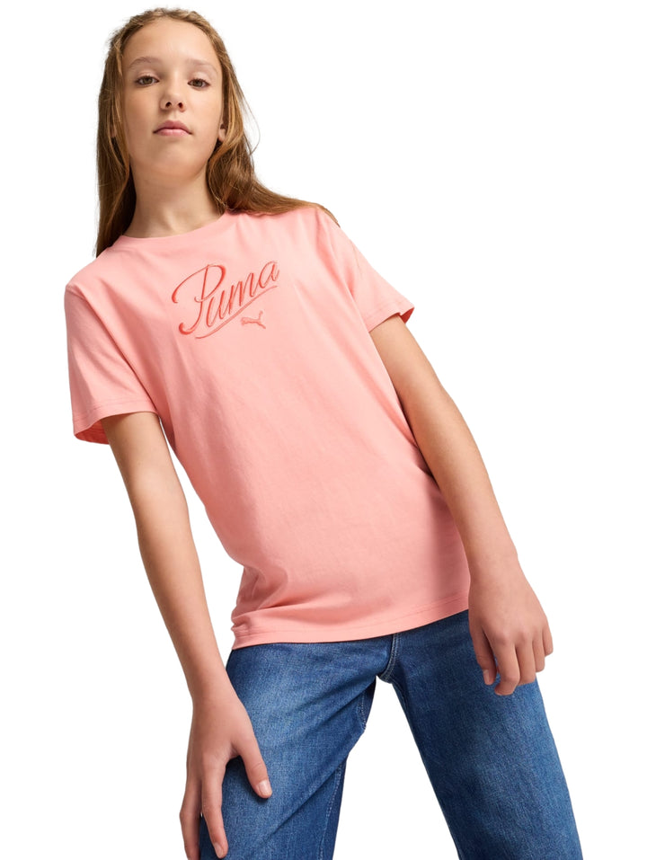 Niña vistiendo una playera Puma de color rosa con logotipo en el pecho y pantalones de mezclilla azules.