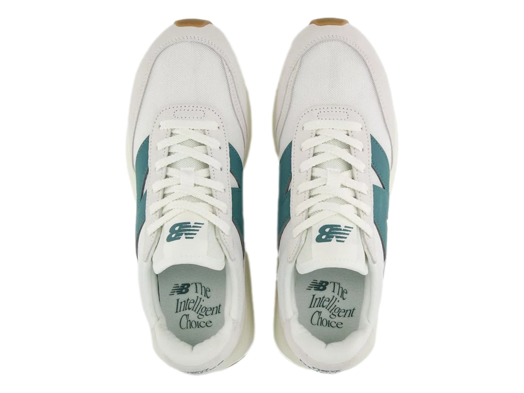 Tenis New Balance blancos con logo verde azulado y suela de goma color café.