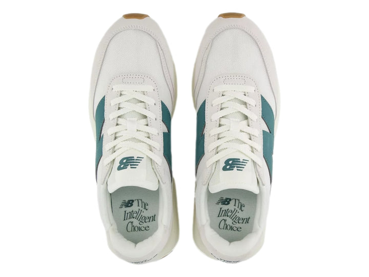 Tenis New Balance blancos con logo verde azulado y suela de goma color café.