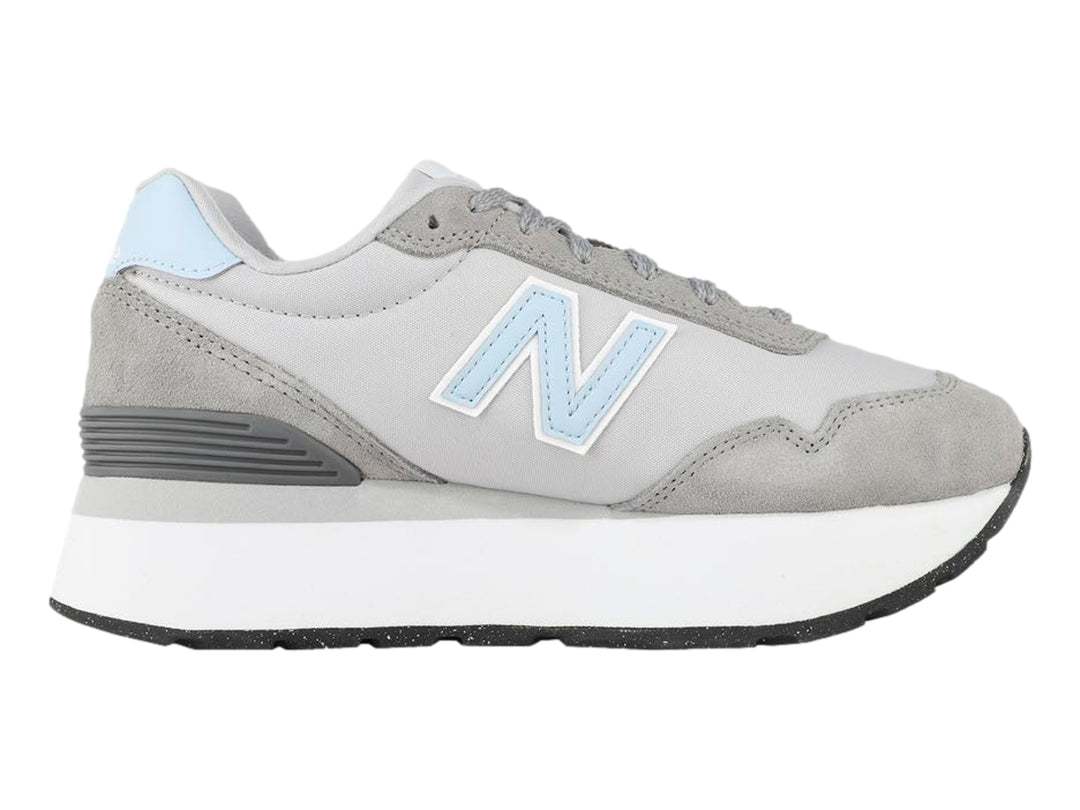 Tenis New Balance color gris con suela blanca de plataforma y detalles en azul claro.