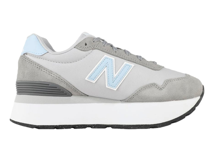 Tenis New Balance color gris con suela blanca de plataforma y detalles en azul claro.