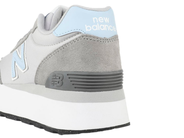 Tenis New Balance color gris con suela blanca de plataforma y detalles en azul claro.