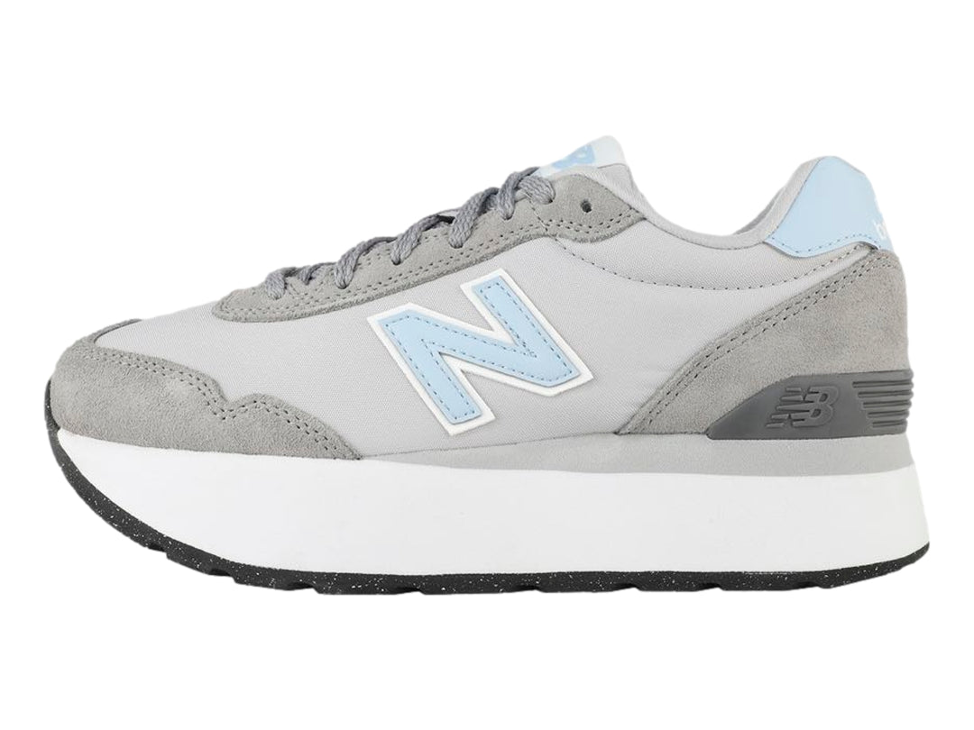 Tenis New Balance color gris con suela blanca de plataforma y detalles en azul claro.