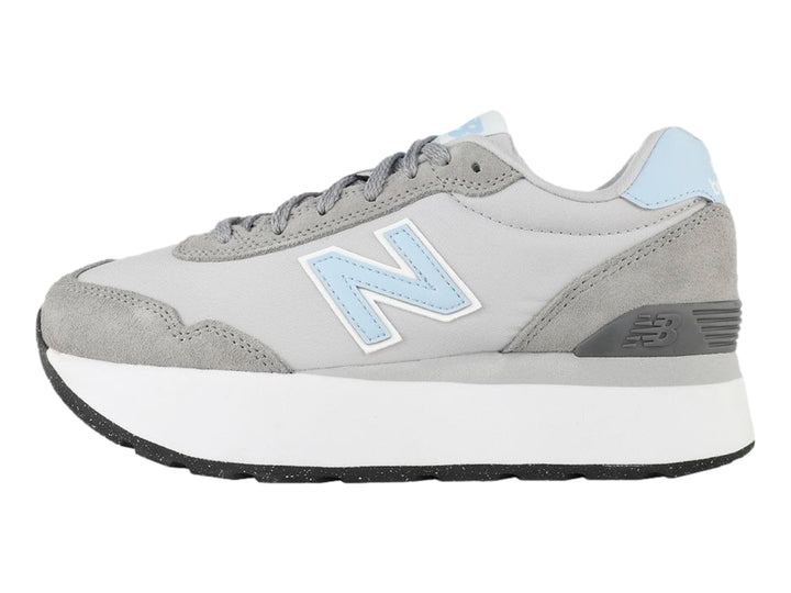 Tenis New Balance color gris con suela blanca de plataforma y detalles en azul claro.