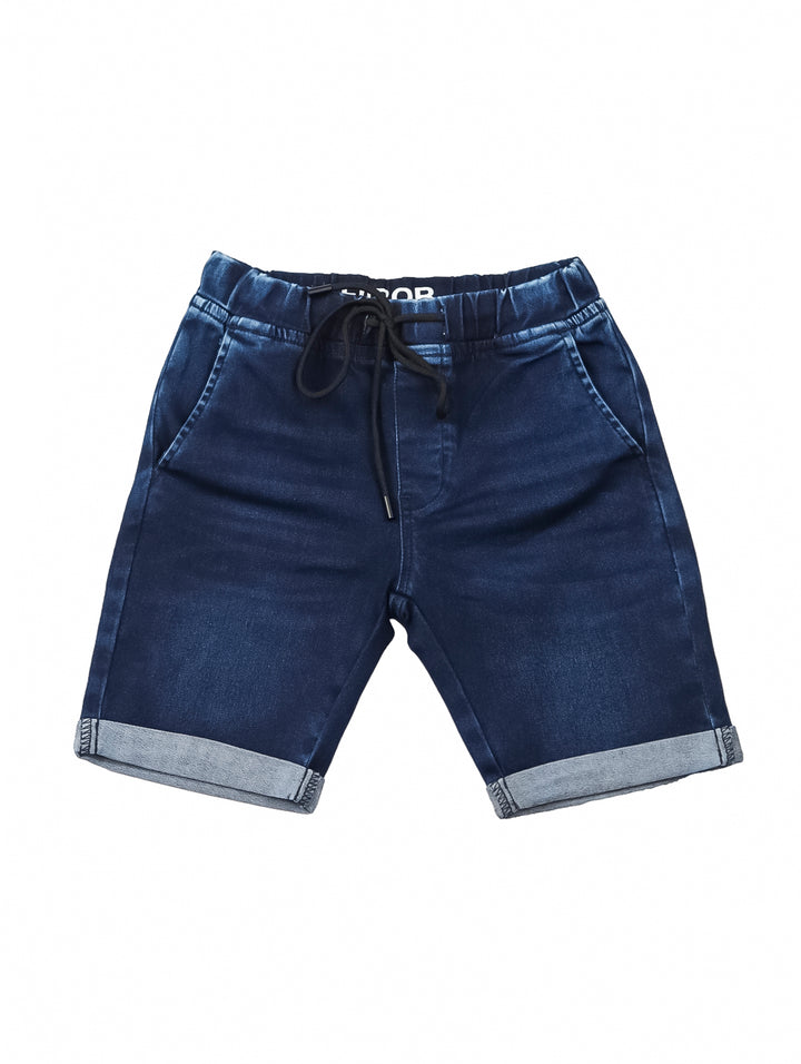 Niño vistiendo shorts de mezclilla azul con cintura elástica y dobles en el ruedo.