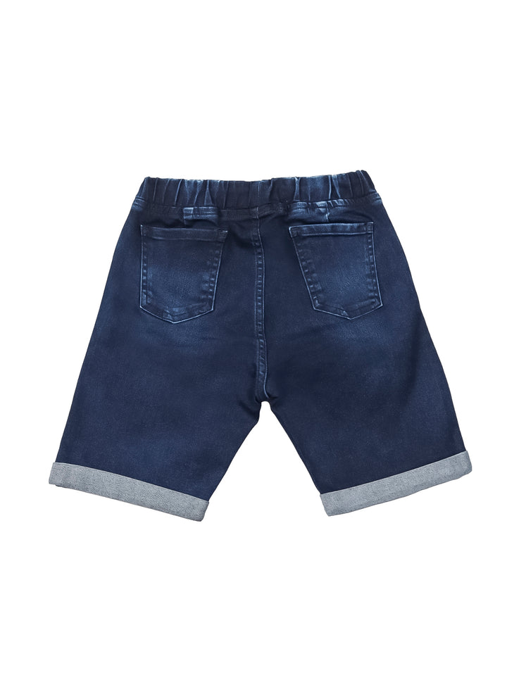 Niño vistiendo shorts de mezclilla azul con cintura elástica y dobles en el ruedo.