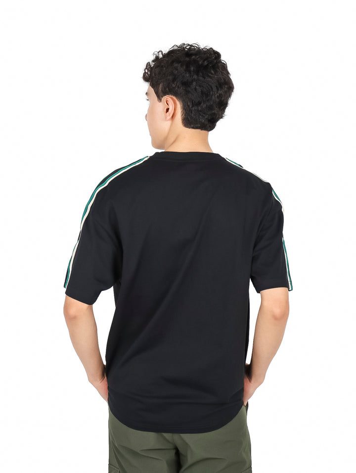 Hombre vistiendo playera YAKUZA color negro con un parche rojo en el pecho y detalles verdes en los hombros.