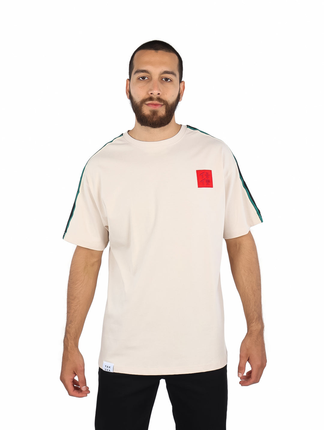 Playera color beige de manga corta con rayas verdes en los hombros y un parche rojo en el pecho.