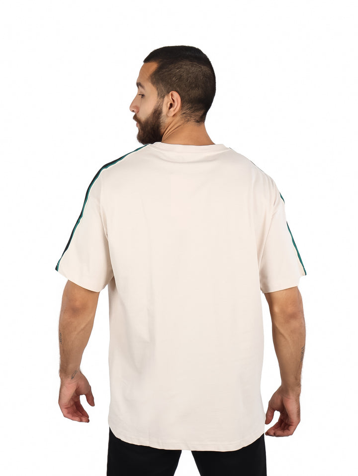 Playera color beige de manga corta con rayas verdes en los hombros y un parche rojo en el pecho.
