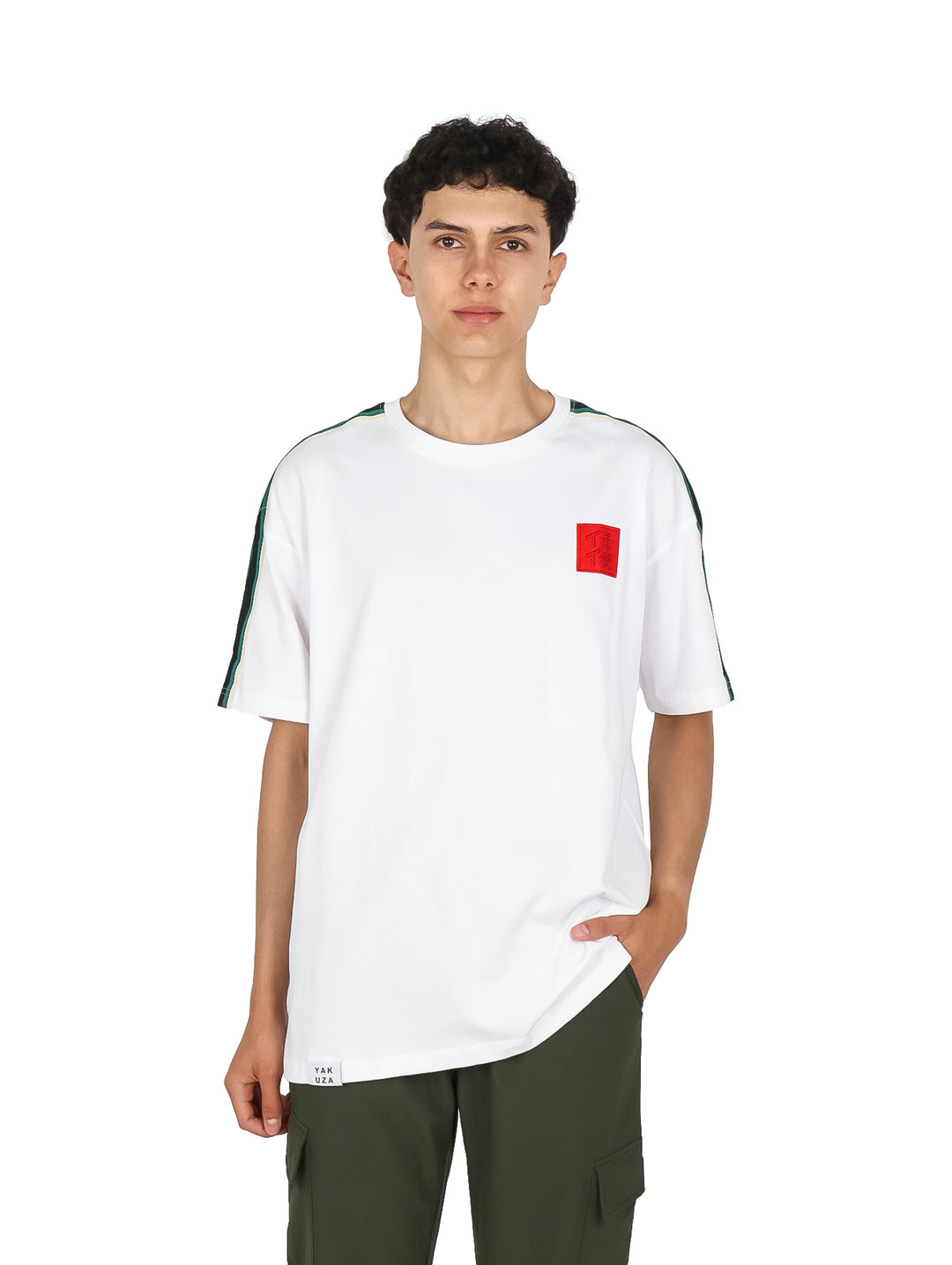 Hombre vistiendo playera blanca de manga corta con un cuadrado rojo en el pecho y franjas verdes en los hombros.